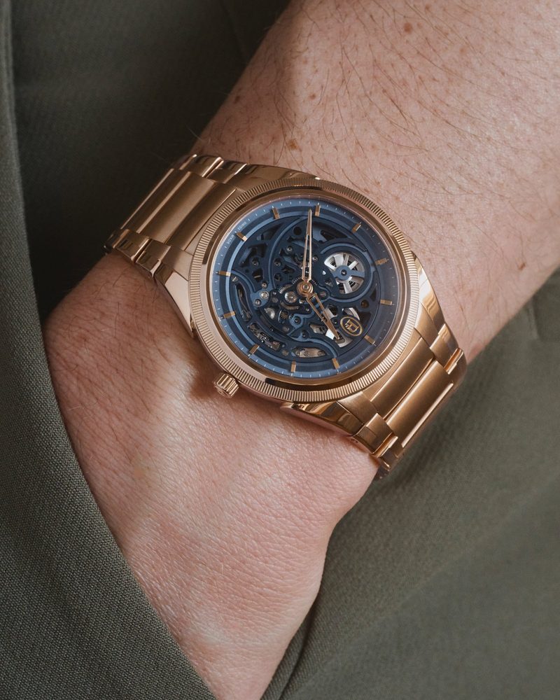 Rose gold watch with a blue skeleton dial, worn on the wrist